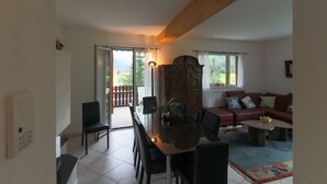 A spacious living area with a dining table, chairs, a sofa, and a large window providing a view of the outdoors. - Apartments Schmid (Davos)