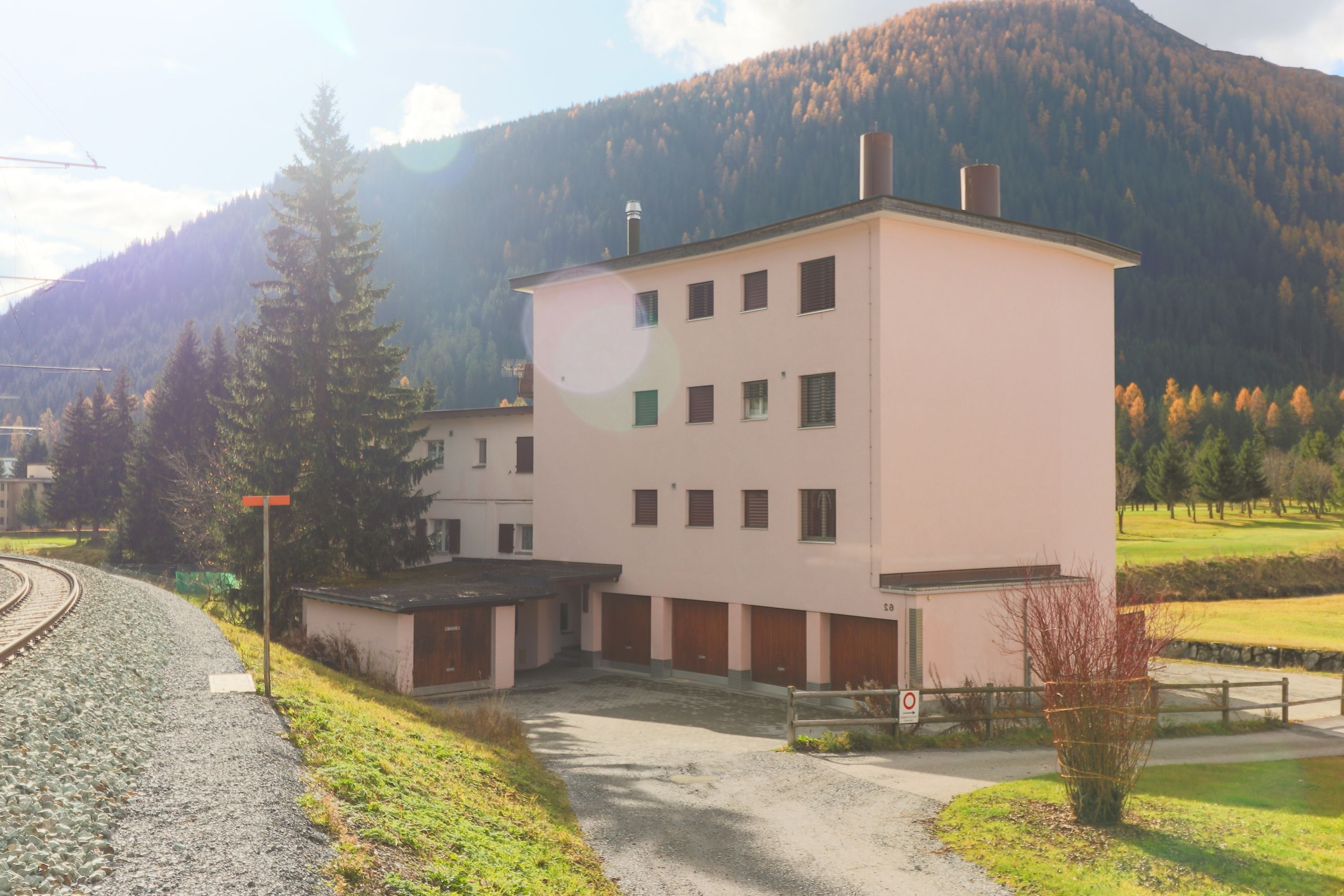 A multi-story building with a flat roof, surrounded by a gravel driveway and a railway track.