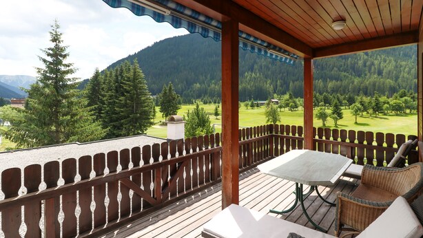 A wooden deck with a table and chairs, overlooking a mountainous landscape. - Apartments Schmid (Davos)