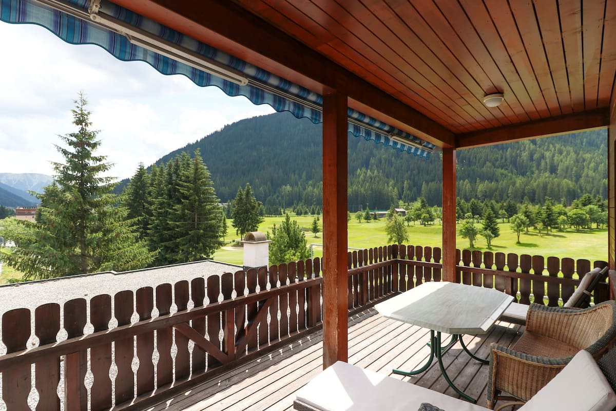 A wooden deck with a table and chairs, overlooking a mountainous landscape.