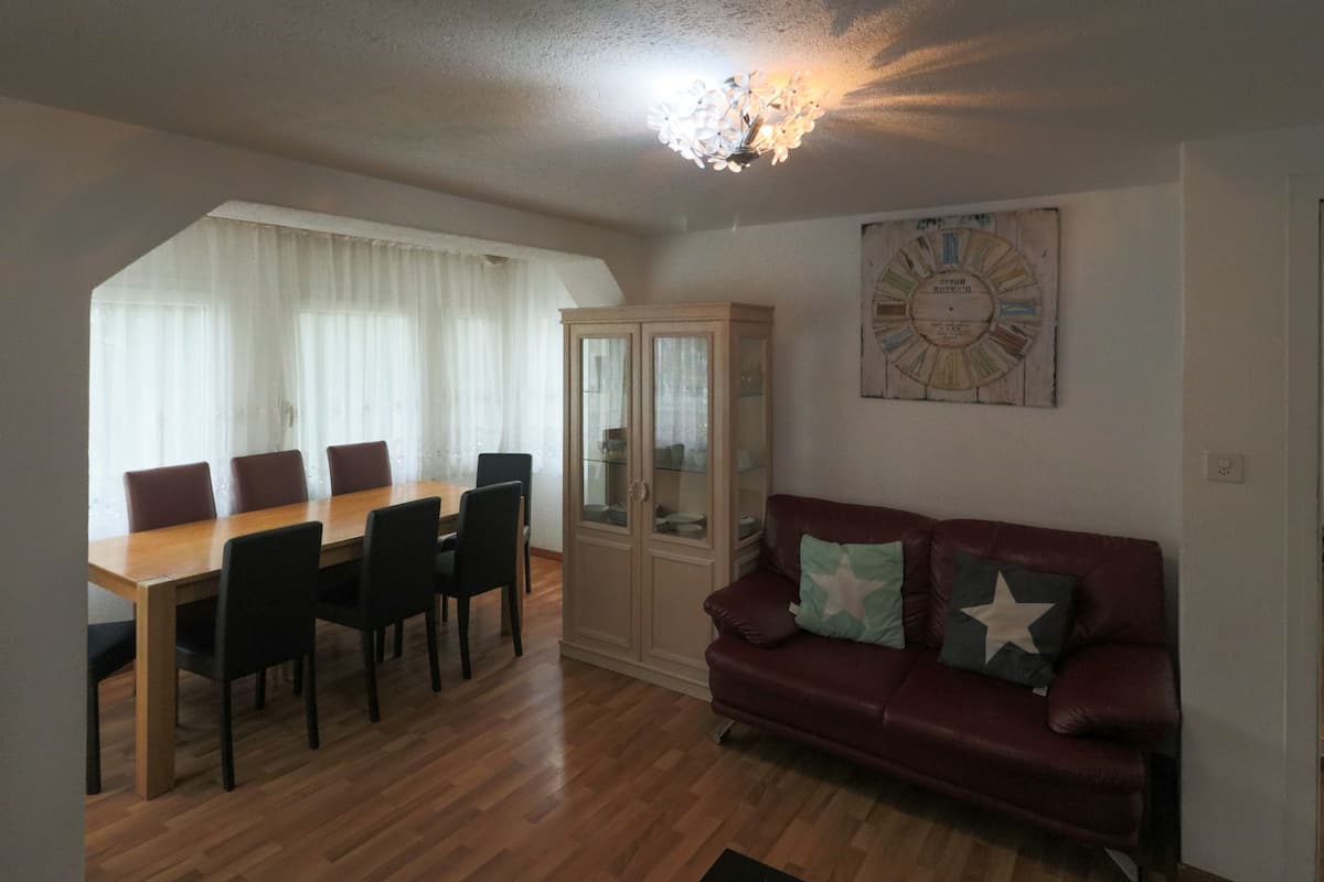 A dining area with a wooden table and chairs, a glass cabinet, and a red leather sofa with cushions.