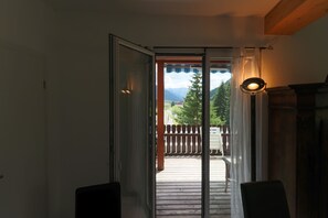 En öppen dörr som leder ut till en balkong med trägolv, utsikt över bergen och en lyktstolpe.