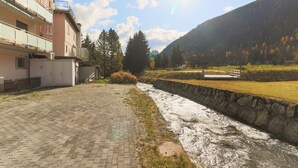 A paved pathway beside a river, a stone wall, and a building with balconies. - Apartments Schmid (Davos)