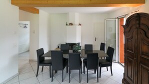 A dining area with a round table and black chairs, a wooden ceiling beam, and a sliding glass door. - Apartments Schmid (Davos)