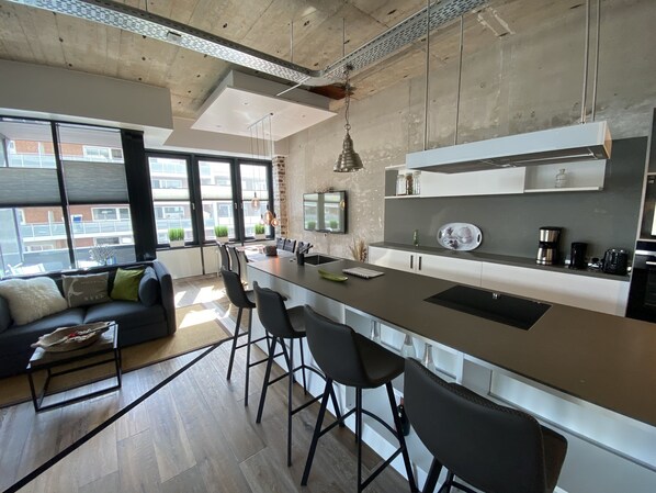 A modern kitchen with a large island, bar stools, and a dining area with a sofa.