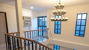 A multi-level interior with a wooden staircase, a chandelier, and large windows. - The Great Winter (Chiang Rai)