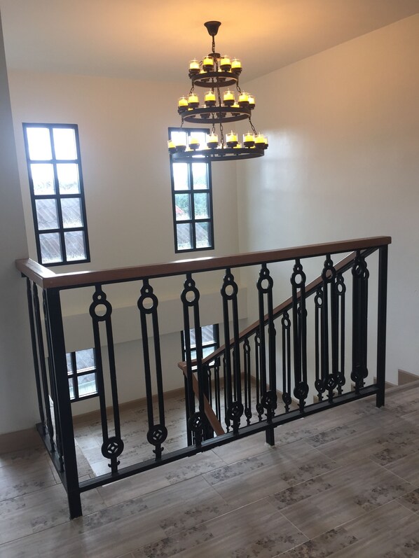 A staircase with a wooden handrail and black wrought iron balusters, leading to a landing with a chandelier.