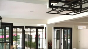 An indoor dining area with white chairs and tables, a pool table, and a glass enclosure with a view of the outside. - The Great Winter (Chiang Rai)