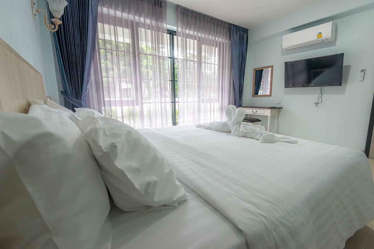 A hotel room with a large bed, a TV, an air conditioner, and a window with curtains.