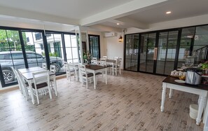 Un vaste espace de salle à manger avec une grande table et des chaises, de grandes fenêtres donnant sur la rue et un aménagement intérieur moderne.
