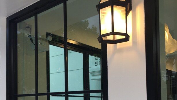 A modern building entrance with a large glass door and a black metal lantern. - The Great Winter (Chiang Rai)