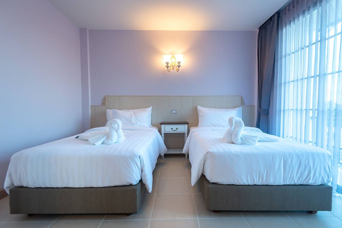 A hotel room with two beds, a nightstand, and a wall-mounted light fixture.