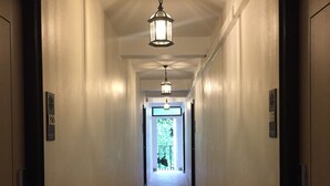 A long, narrow hallway with a wooden floor and white walls. There are two doors on each side, and a light fixture hangs from the ceiling. - The Great Winter (Chiang Rai)