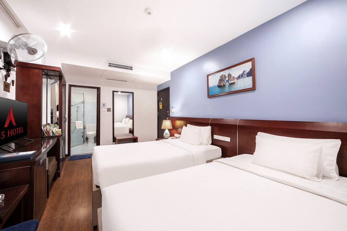 Une chambre d’hôtel avec deux lits, une télévision, un bureau et une salle de bain visible à travers une porte ouverte.