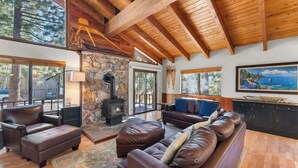 A spacious living room with a stone fireplace, leather sofas, and a large painting of a coastal scene. - Hot Tub! Gas Fireplace! Two Decks, Garage, New Flooring, Pets OK! (Kings Beach)