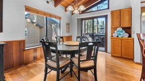 A wooden dining table with chairs, a kitchen area with wooden cabinets, and large windows. - Hot Tub! Gas Fireplace! Two Decks, Garage, New Flooring, Pets OK! (Kings Beach)
