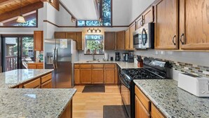 A modern kitchen with wooden cabinets, granite countertops, a stainless steel refrigerator, a stove, and a microwave. - Hot Tub! Gas Fireplace! Two Decks, Garage, New Flooring, Pets OK! (Kings Beach)