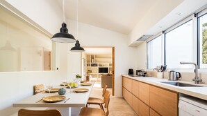 Una cocina moderna con armarios de madera, un comedor con una mesa larga y sillas, y un ventanal que proporciona luz natural.