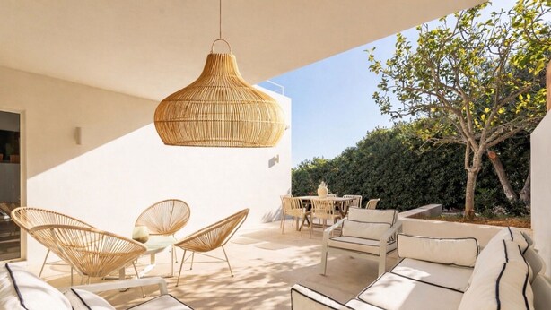 Un patio exterior con mobiliario de mimbre, una lámpara colgante y vistas a un seto y un árbol.