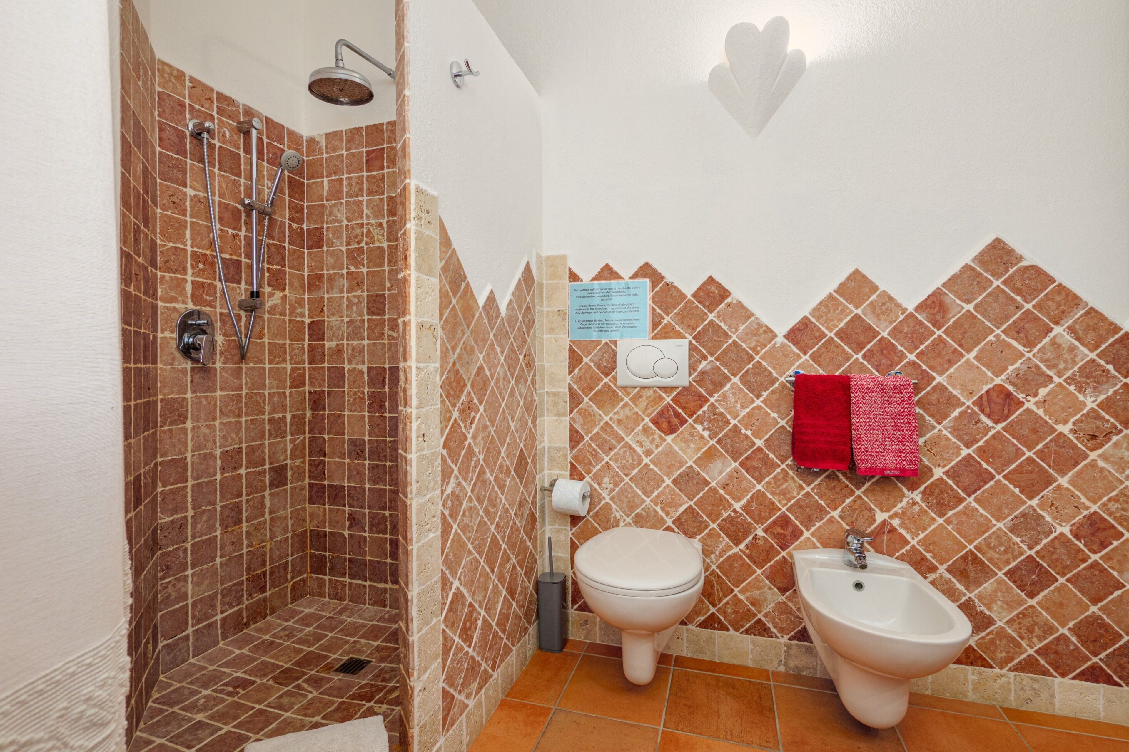 A bathroom with a shower, toilet, bidet, and tiled walls.