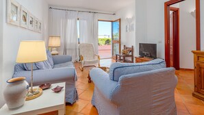 A living room with striped sofas, a table with a lamp, a TV, and a door leading outside. - Apartment "Casa Erica" with Sea View, Wi-Fi & Private Terrace (Palau)