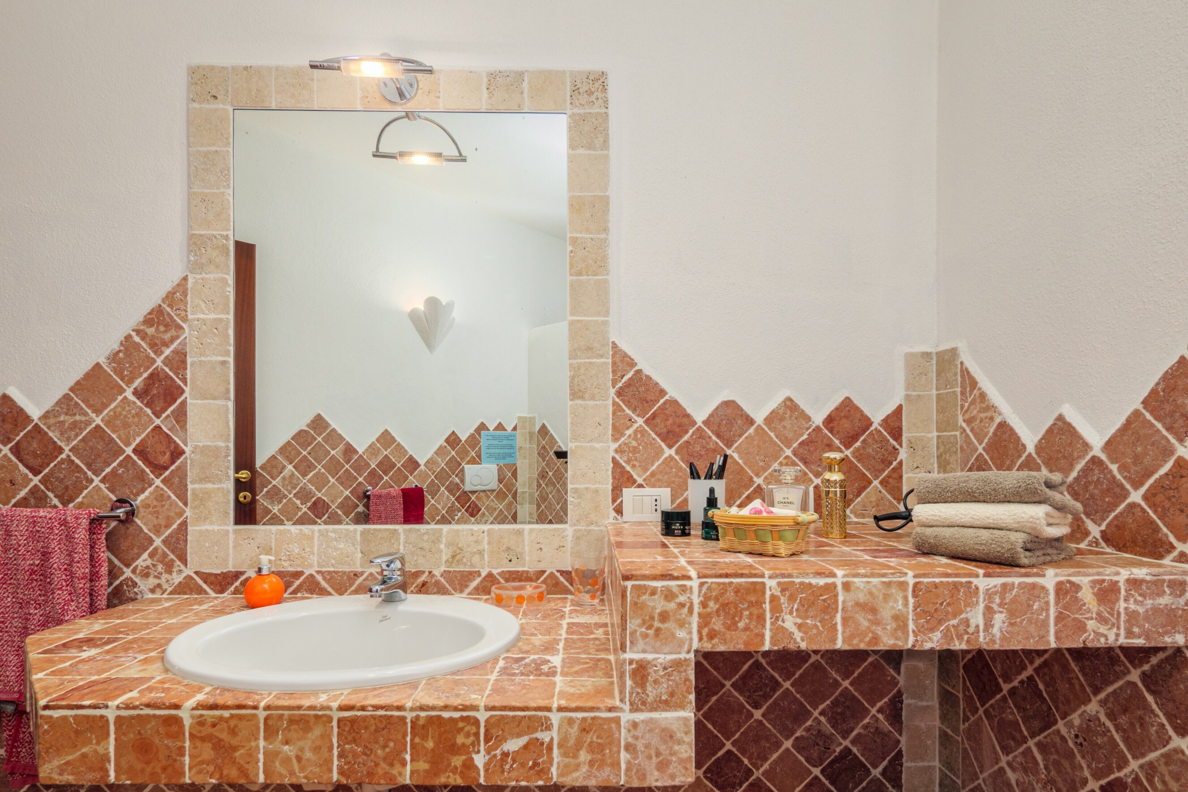 Un baño con lavamanos blanco, espejo y pared con azulejos.