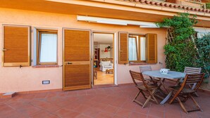 An outdoor patio with a table and chairs, a sliding glass door entrance, and a small indoor space visible through the door. - Apartment "Casa Erica" with Sea View, Wi-Fi & Private Terrace (Palau)