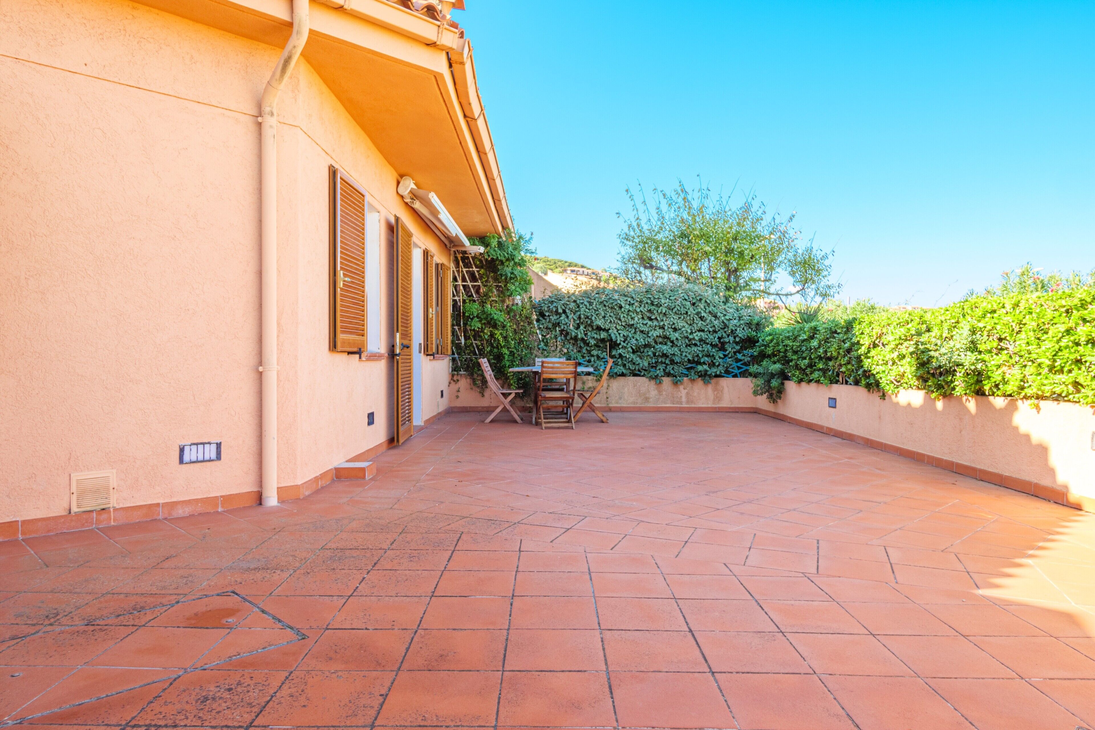 A courtyard with a tiled floor, a table with chairs, and a building with shutters.