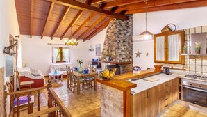 A kitchen with a stone wall, wooden beams, a dining area with a table and chairs, and a bar area with a counter.
