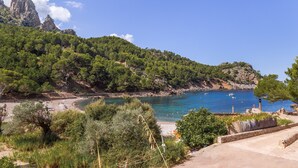 A coastal landscape with a beach, rocky cliffs, and a clear blue sky.