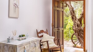 A bedroom with a wooden bed, a dresser, a painting, and a view of a tree through an open door.