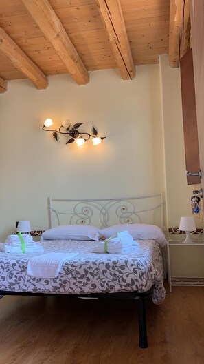 Un dormitorio con techo de madera, una cama con ropa de cama estampada, dos mesitas de noche con lámparas y un aplique en la pared.