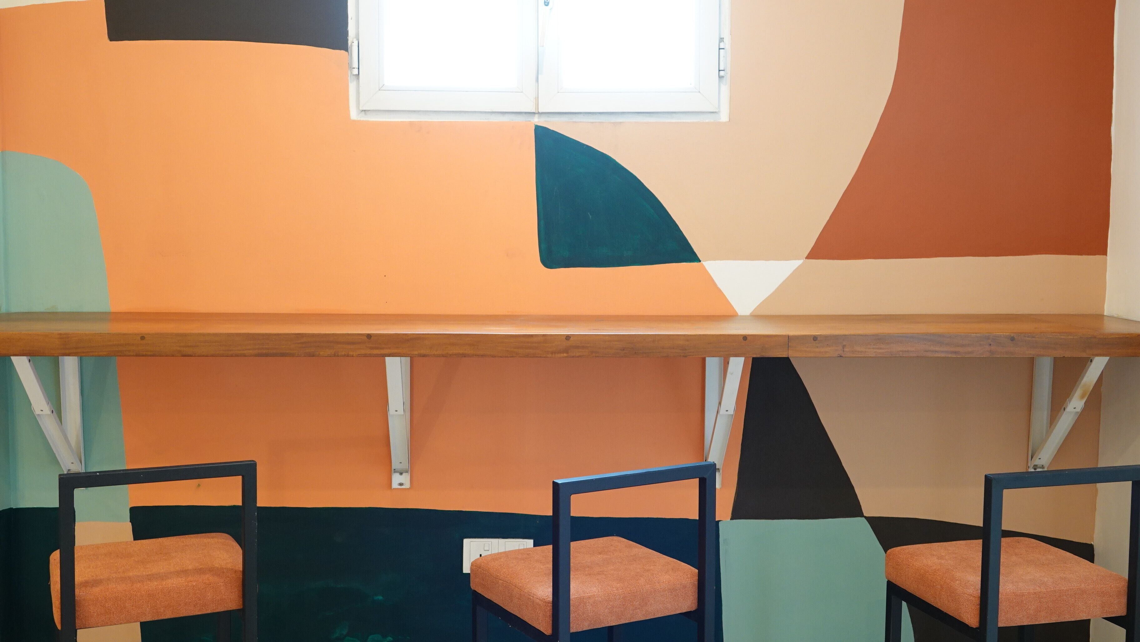A room with a long wooden table and three chairs with orange cushions.