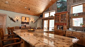 Una cocina amplia con una gran isla de granito, armarios de madera y techo rústico.
