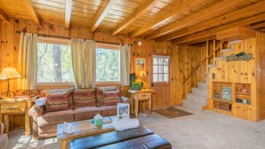 A cozy log cabin interior with a wooden staircase, a sofa with patterned cushions, and a welcoming sign. - Big Bear Retreat - 2 Fireplaces, Deck, Barbecue, Fenced Yard (Big Bear Lake)