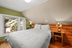 Een slaapkamer met een groot bed, houten hoofdeinde, bedlampje en uitzicht op een tuin door een raam.