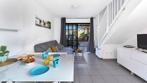Un espace de vie moderne comprenant un coin repas, un canapé et un téléviseur posé sur un meuble blanc.