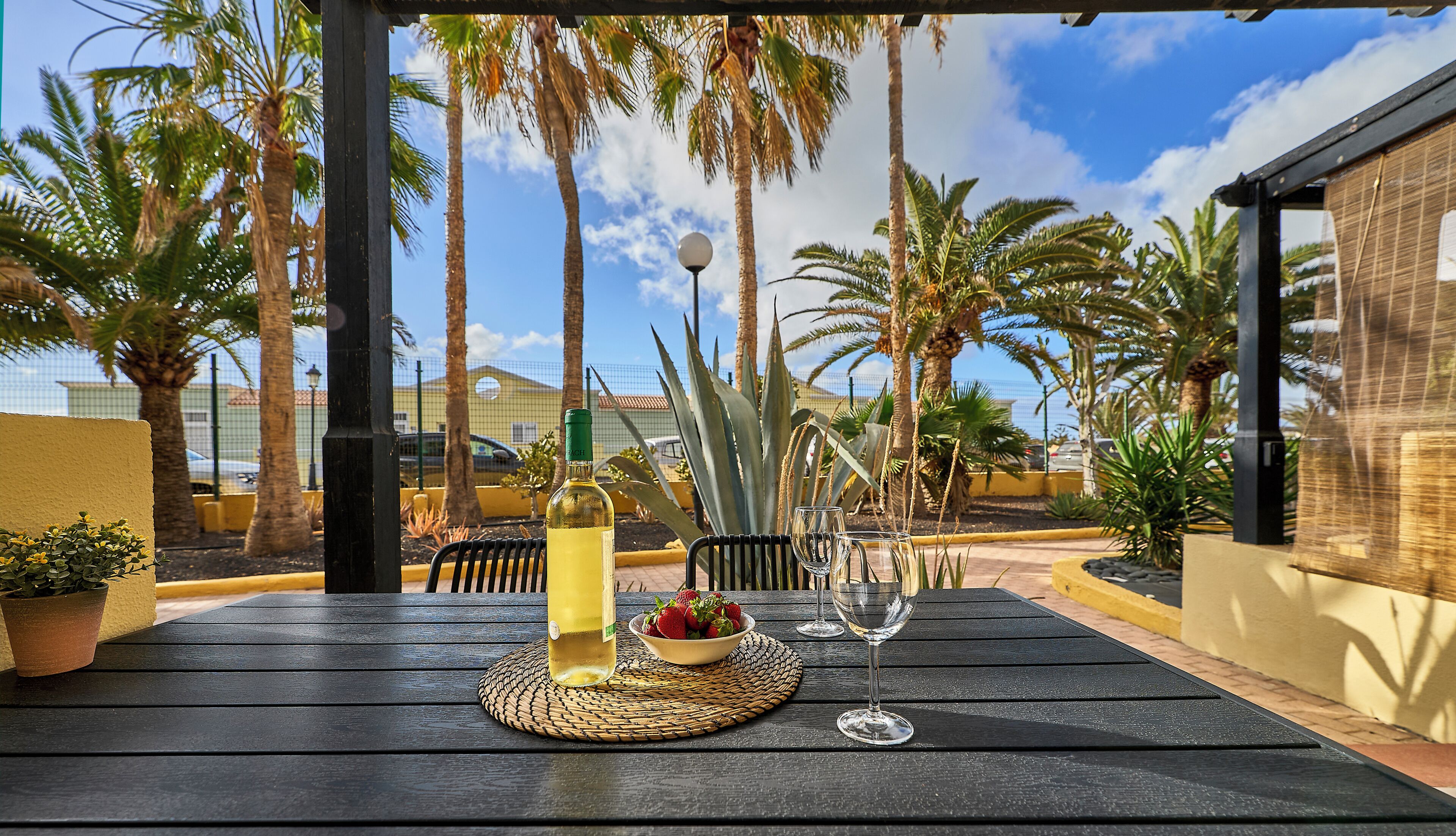 An outdoor patio with a table set for two, featuring a bottle of white wine, a bowl of strawberries, and a wine glass.
