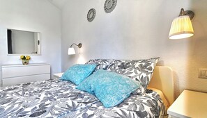 Une chambre à coucher comprenant un lit, une table de chevet, une lampe, un miroir et un luminaire fixé au mur.