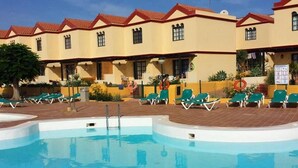 A swimming pool with lounge chairs and a building with red-tiled roofs.