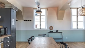 A modern kitchen with a wooden table, black chairs, a black refrigerator, and a window with curtains. - PHILIPPE AUGUSTE LOFT 4 - Loft for 12 - 5 rooms - BASTILLE - PÈRE LACHAISE (Paris)