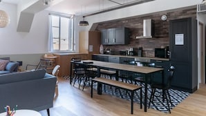 A modern kitchen with a large island, dark cabinetry, and a brick accent wall. - PHILIPPE AUGUSTE LOFT 4 - Loft for 12 - 5 rooms - BASTILLE - PÈRE LACHAISE (Paris)