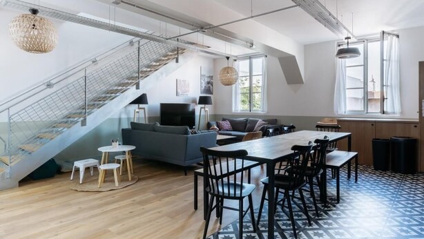 A spacious living area with a staircase, a sofa set, a dining table with chairs, and a patterned floor. - PHILIPPE AUGUSTE LOFT 4 - Loft for 12 - 5 rooms - BASTILLE - PÈRE LACHAISE (Paris)