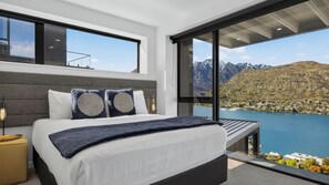 A modern bedroom with a large bed, a view of a lake, and mountains in the background. - Woods Villa Tui (Queenstown)