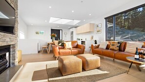 A modern living room with a fireplace, leather sofas, ottomans, and a large window offering a view of the outdoors. - Woods Villa Tui (Queenstown)