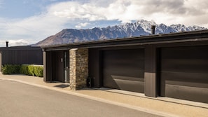 A modern building with a garage door, a stone pillar, and a mountain backdrop. - Woods Villa Tui (Queenstown)