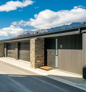 A modern building with stone pillars, numbered garage doors, and a mountain backdrop. - Woods Villa Tui (Queenstown)