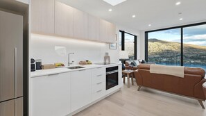 A modern kitchen with white cabinetry, a built-in oven, and a large window offering a scenic view of hills and a lake. - Woods Villa Tui (Queenstown)