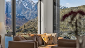 A room with a large window offering a mountain view, a sofa with a plaid throw, and a vase with a plant. - Woods Villa Tui (Queenstown)