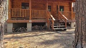 Une cabane rustique en rondins de bois, dotée d’un porche en bois et d’un escalier menant à l’entrée.